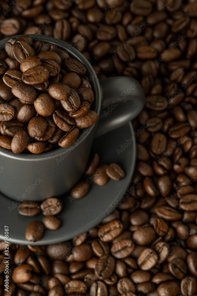 Fototapeta premium Cup and saucer with coffee beans on coffee background. View from above close-up.