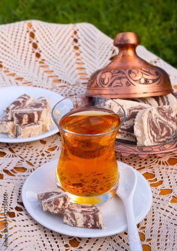 Photos Turkish tea in a glass Cup and marble halva on a table with a handmade tableclot