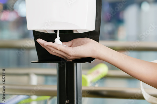 Foto boy's hand under automatic foam dispenser before go inside with blurred shopping
