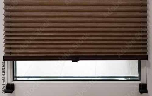 Pleated blinds close up on the window in the interior. Home blinds - cordless pleated modern shades on apartment windows. Brown color fabric. photo