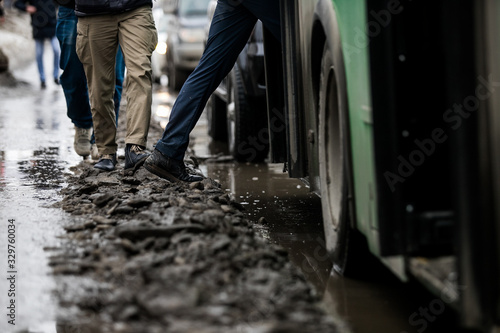 people are standing at a bus stop, getting on a bus stepping over uncleared snow and mud, special services do not clean the city