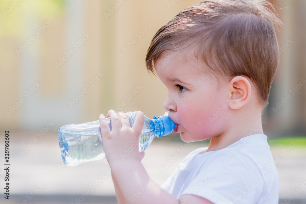 handsome boy drinks clear water from a bottle on a sunny day outside