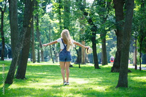 young beautiful girl in denim overalls and a light hat walking in the park