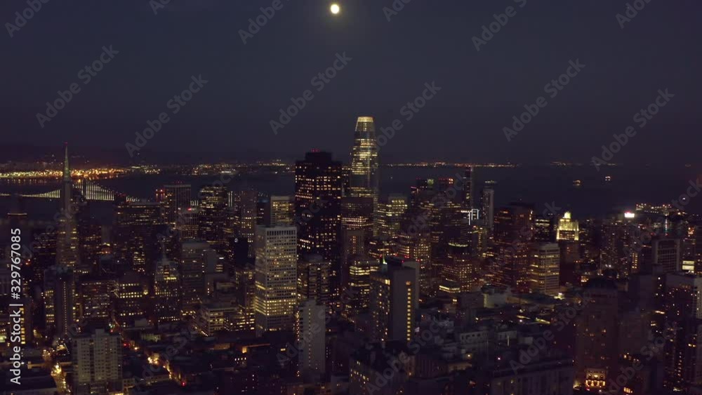 Aerial, tilt up, drone shot overlooking downtown San Francisco cityscape, revealing the full moon, during night time, in California, United States Aerial, tilt up, drone shot overlooking downtown San Francisco cityscape, revealing the full moon, during night time, in California, United States