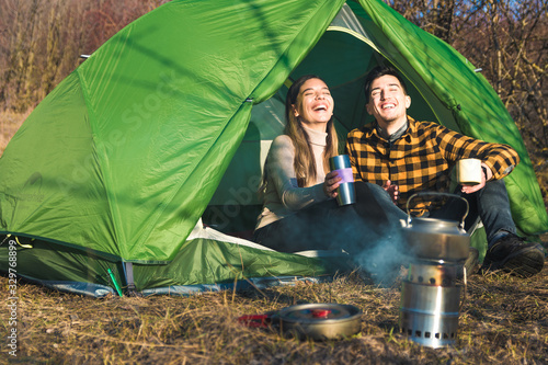 young couple enjoying outdoors camping in nature with tent drink tea by a campfire
