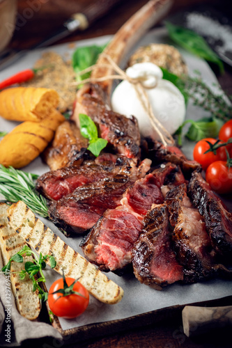 Tomahawk grilled steak cut into pieces with vegetables on a wooden Board, cooking meat barbecue