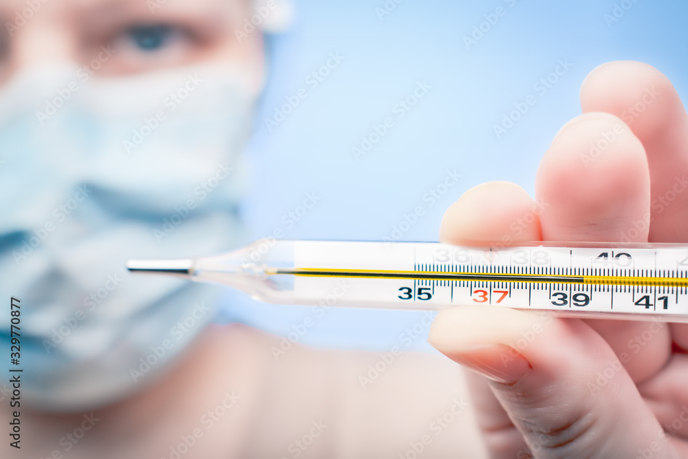 Overheated thermometer in a woman's hand in a protective mask: concept of an epidemic of coronovirus or flu Overheated thermometer in a woman's hand in a protective mask: concept of an epidemic of coronovirus or flu
