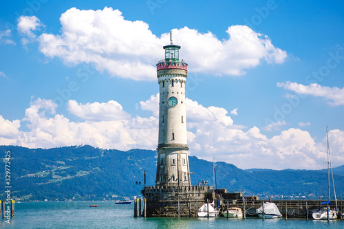 Lindau, Bavaria, Germany. Old lighthouse with clock in bay. Antique bavarian town at Lake Constance Bodensee. Monument at entrance to port, yachts by piers. Summer landscape.