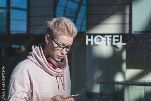 Portrait of a beautiful blonde woman with headphones and glasses, looking at the departure schedule in the phone