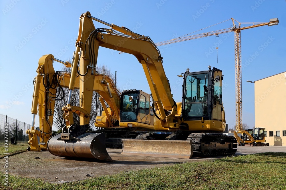 Brand new excavators parked on the roadside. Tower crane on background Brand new excavators parked on the roadside. Tower crane on background