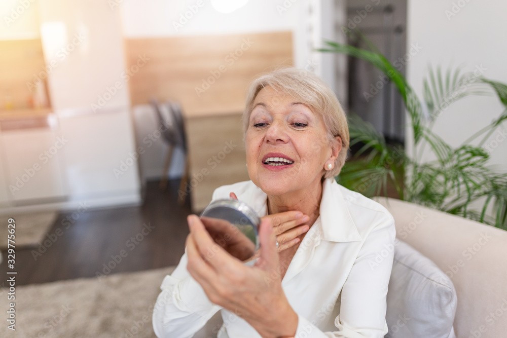 Charming, pretty, old woman touching her perfect soft face skin with fingers, smiling at camera over gray background, using day, night face cream, cosmetology procedures Charming, pretty, old woman touching her perfect soft face skin with fingers, smiling at camera over gray background, using day, night face cream, cosmetology procedures