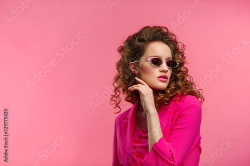 Close up fashion studio portrait of young beautiful women with curly hair.Nice girl with wavy hairstyle bright make up and stylish eyeglasses isolated over pink background.Beauty and hair care concept