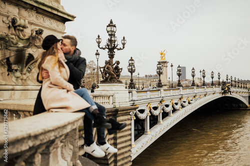 Amazing stylish couple sitting and embracing at Pont Alexandre-III. Paris, France. Happy romantic couple in Paris near the famous Alexandre III bridge over the Seine. Kiss, love. © eduard