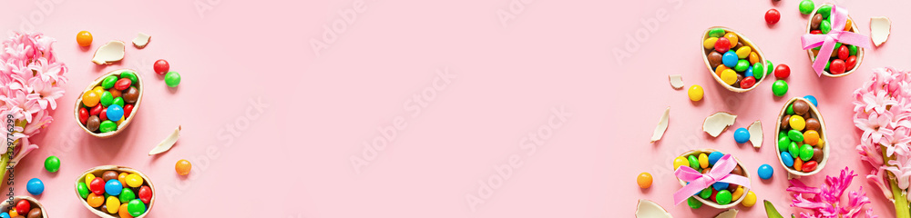 Chocolate Easter eggs and colorful candies on pastel pink paper background. flat lay, top view, overhead, copy space, template, mockup. Horizontal banner for web design