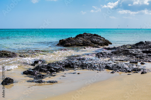The tropical and paradisiacal landscape of a beach with blond sand and turquoise sea with black rocks.