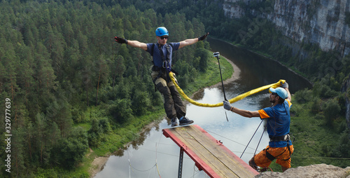 Photos Young man jumping with a rope from a great height into the deep canyon on the background of the forest and river below, panorama