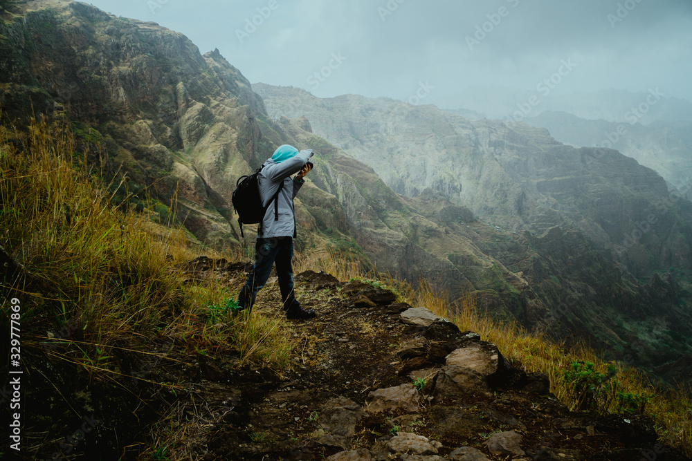Hiker with camera in the steep mountainous terrain shooting a foto of lush canyon valley on the path from Xo-Xo Valley. Santo Antao Island, Cape Verde