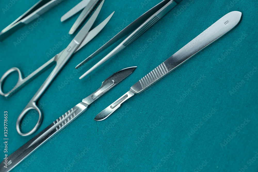 Basic surgical instrument scalpel forceps tweezers scissors spread on surgical green drape fabric Basic surgical instrument scalpel forceps tweezers scissors spread on surgical green drape fabric