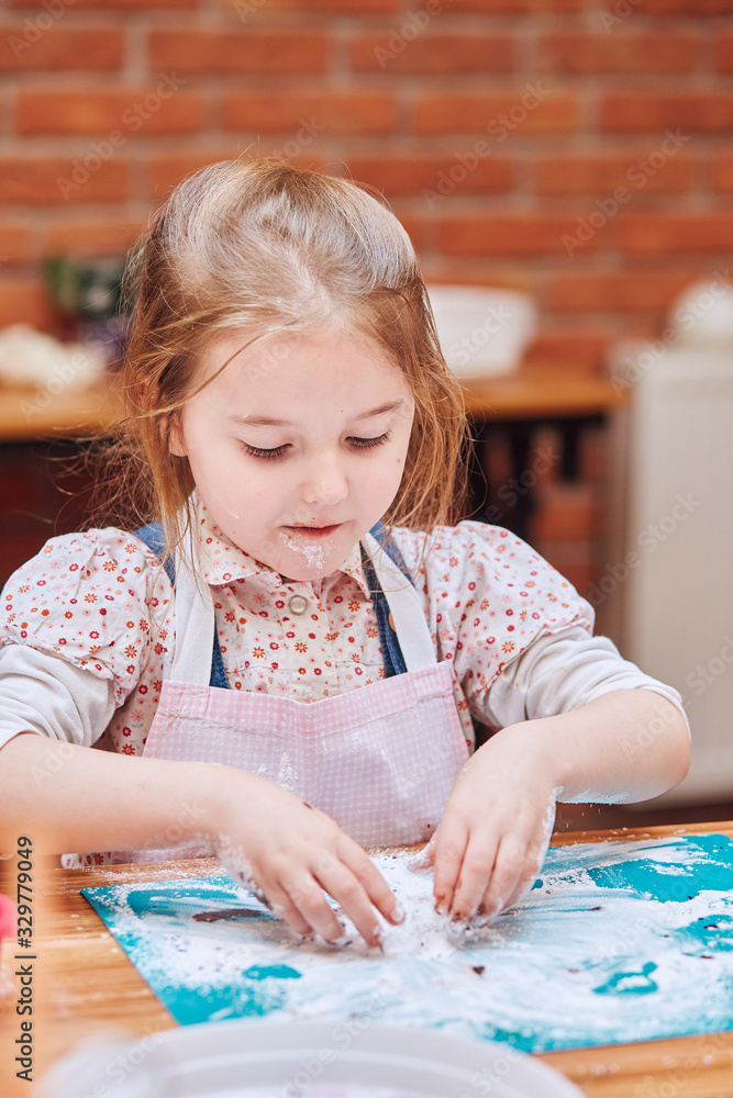Little girl eating the icing sugar left after baking cookies. Kid taking part in baking workshop. Baking classes for children, aspiring little chefs. Learning to cook Little girl eating the icing sugar left after baking cookies. Kid taking part in baking workshop. Baking classes for children, aspiring little chefs. Learning to cook