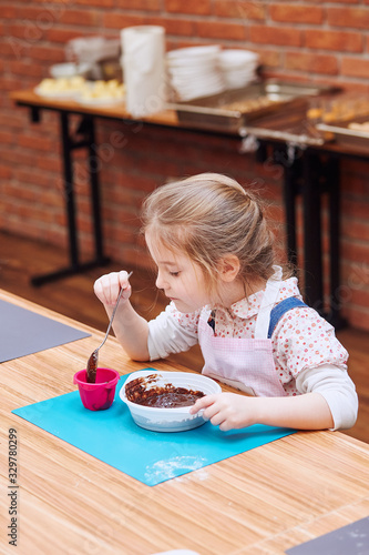 Принти на полотні Little girl putting the melted chocolate and cocoa to cupcake