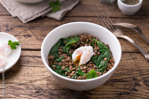 Boiled lentils with spinach, herbs, spices and poached egg in ceramic bowls on a wooden background