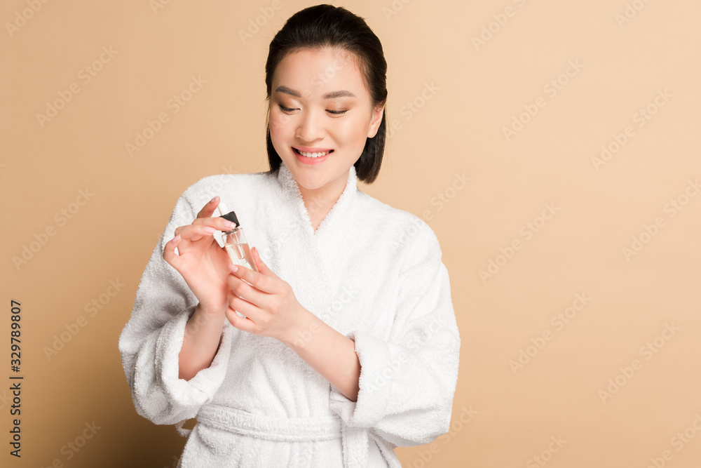 smiling beautiful asian woman in bathrobe holding dropper and bottle with serum on beige background smiling beautiful asian woman in bathrobe holding dropper and bottle with serum on beige background