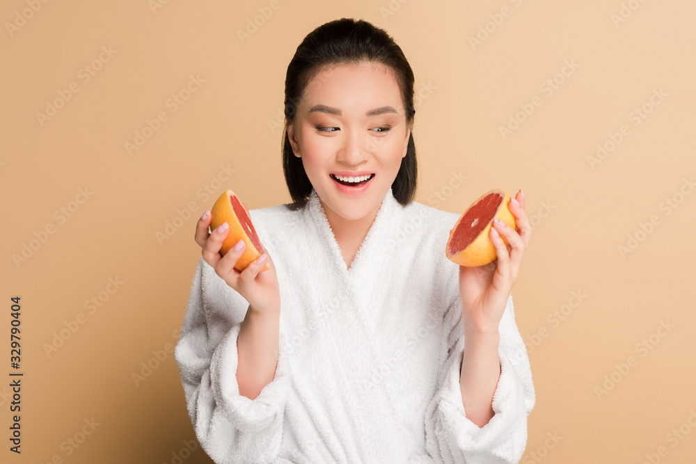 happy beautiful asian woman in bathrobe with grapefruit halves on beige background happy beautiful asian woman in bathrobe with grapefruit halves on beige background