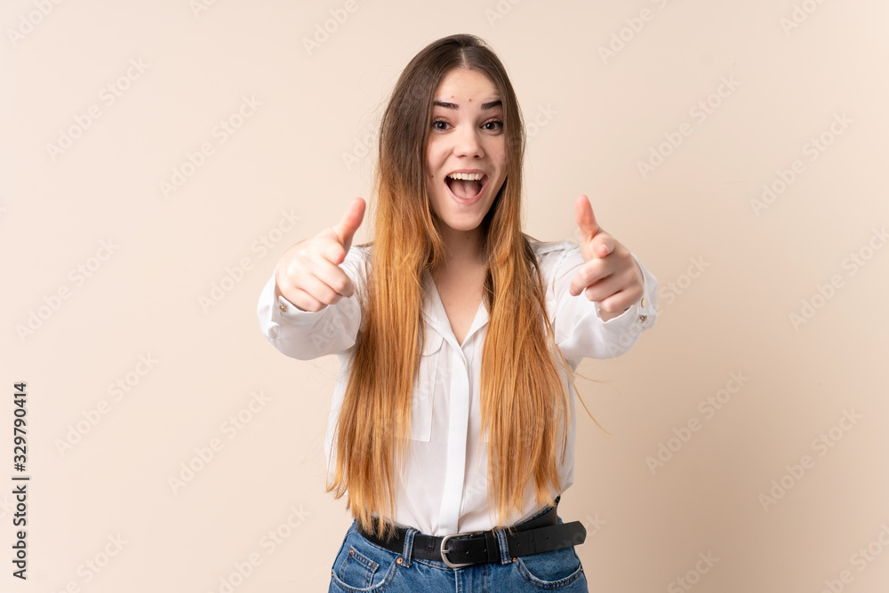 Young caucasian woman isolated on beige background surprised and pointing front Young caucasian woman isolated on beige background surprised and pointing front