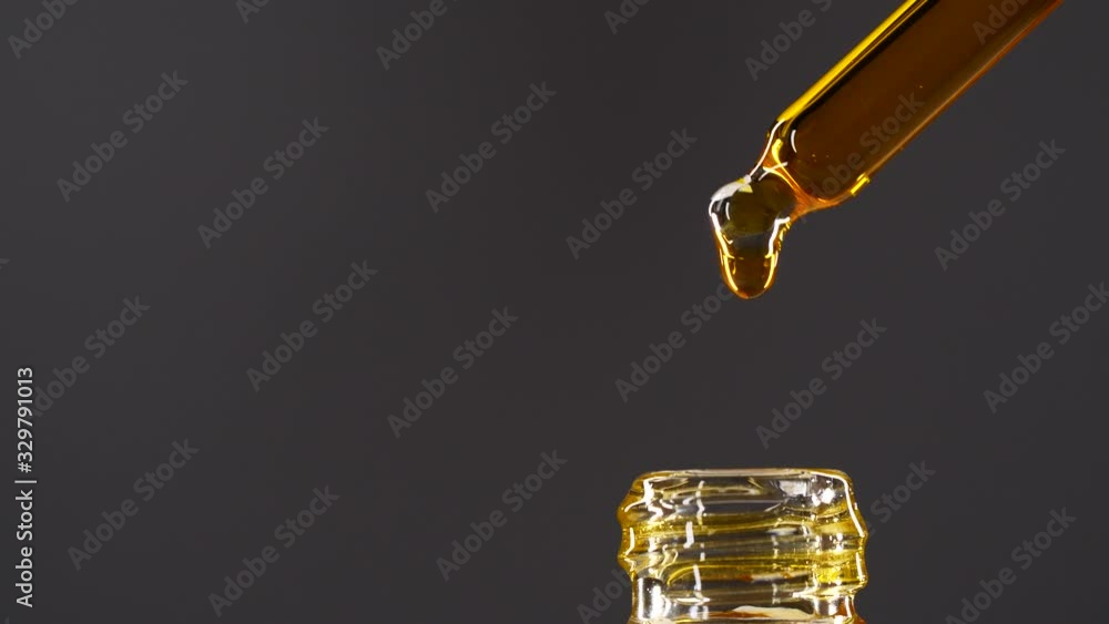 Close-up of of aromatheraphy oil drops dripping from dropper into a bottle, anti aging serum skin care