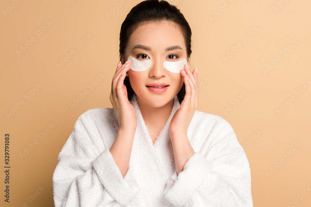 beautiful asian woman in bathrobe with eye patches on face on beige background beautiful asian woman in bathrobe with eye patches on face on beige background