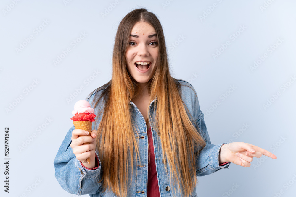 Young woman with a cornet ice cream isolated on blue background surprised and pointing finger to the side Young woman with a cornet ice cream isolated on blue background surprised and pointing finger to the side