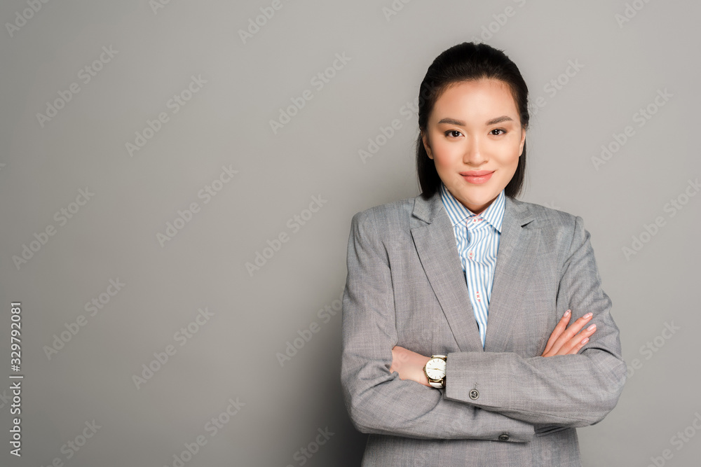 smiling young businesswoman in suit with crossed arms on grey background smiling young businesswoman in suit with crossed arms on grey background