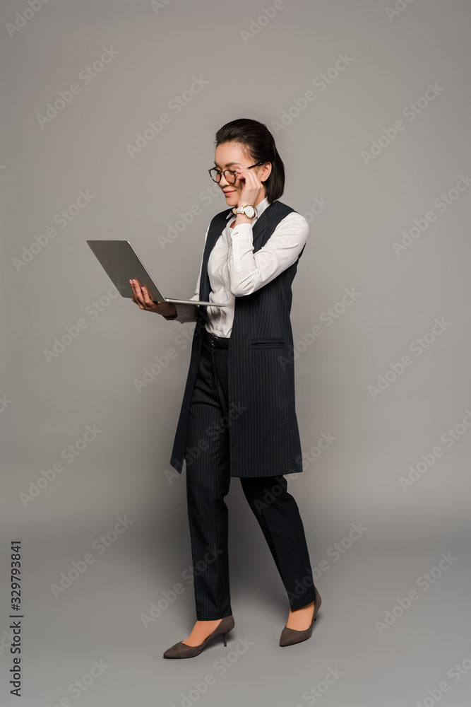 young businesswoman in eyeglasses using laptop on grey background young businesswoman in eyeglasses using laptop on grey background