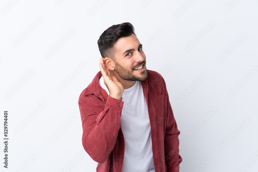 Young handsome man with beard wearing a corduroy jacket over isolated white background listening to something by putting hand on the ear Young handsome man with beard wearing a corduroy jacket over isolated white background listening to something by putting hand on the ear