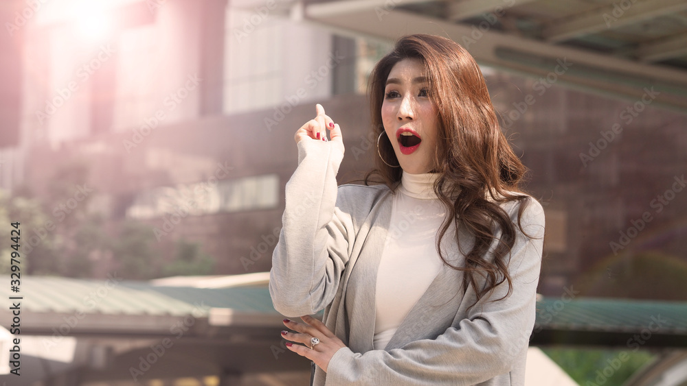 Fototapeta premium Asian business woman standing and finger up like a eureka action and feeling happy which represent have a brilliant idea, thoughtful, solve problem, imagination, inspiration or clever moment in work