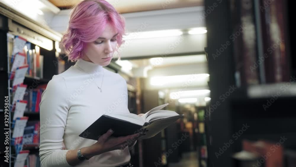 Modern female student in a library is studying a book Modern female student in a library is studying a book