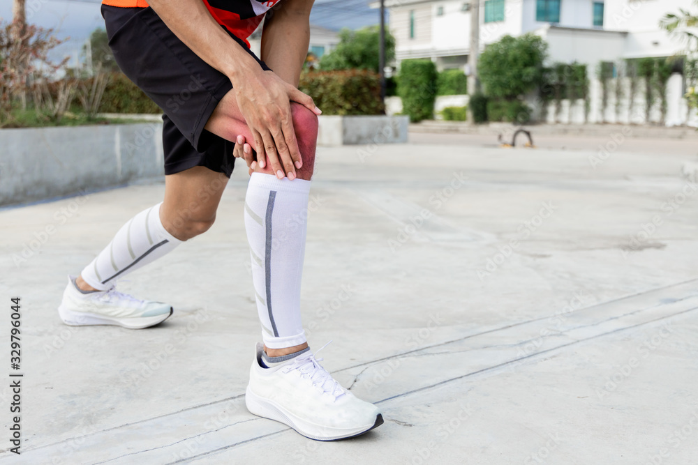 Close up on knee Injury. The man use hands hold on his knee while running in the park. space for text or design. highlight on injured area Close up on knee Injury. The man use hands hold on his knee while running in the park. space for text or design. highlight on injured area