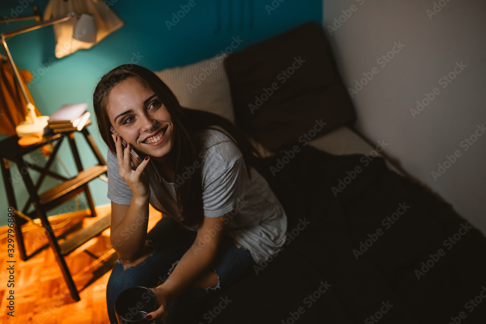 Fototapeta premium young woman using mobile phone in her room. evening scene