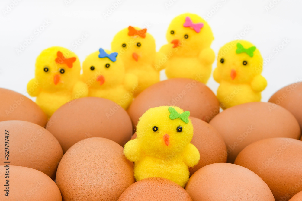 Close up of a yellow chick made of foam sitting among a clutch of fresh brown eggs. In the background are other model chicks.