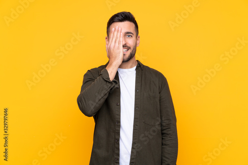 Photos Man over isolated yellow background covering a eye by hand