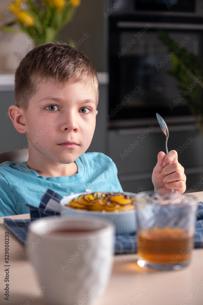 Cute boy sitting at the table and eating oatmeal porridge. Happy child have a breakfast Cute boy sitting at the table and eating oatmeal porridge. Happy child have a breakfast