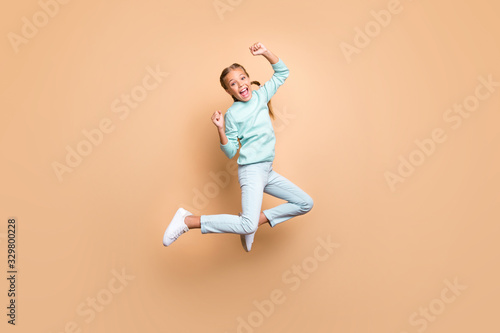 Full body profile photo of beautiful funny little lady jumping high up celebrating winning raise fists wear blue sweater jeans footwear isolated beige color background