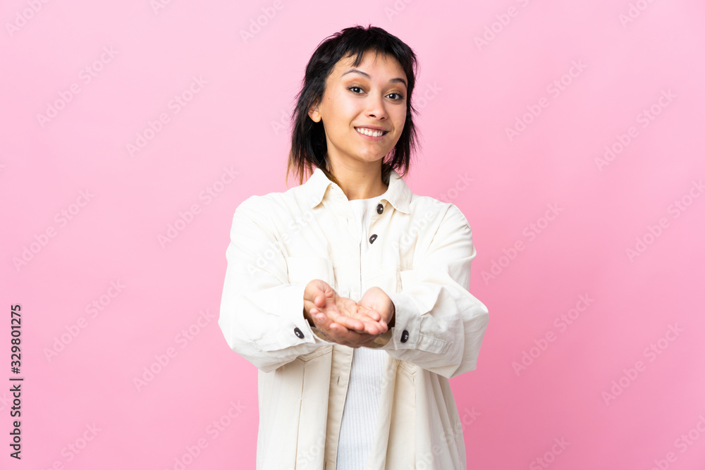 Young Uruguayan woman over isolated pink background holding copyspace imaginary on the palm to insert an ad Young Uruguayan woman over isolated pink background holding copyspace imaginary on the palm to insert an ad