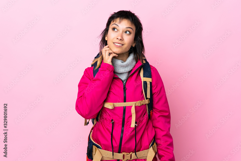 Young mountaineer girl with a big backpack over isolated pink background thinking an idea