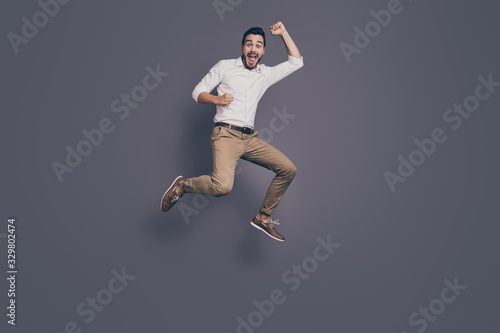 Full length photo of young handsome business man jumping high up rejoicing celebrating new startup project success wear white shirt pants footwear isolated grey color background