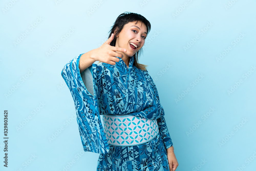 Young woman wearing kimono over isolated blue background with thumbs up because something good has happened Young woman wearing kimono over isolated blue background with thumbs up because something good has happened
