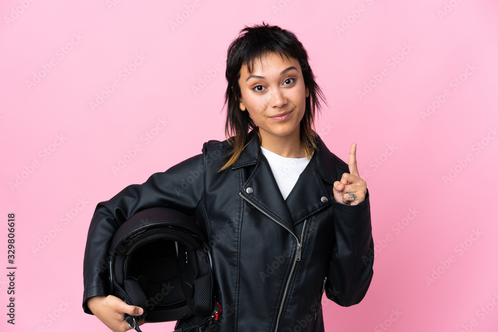 Young Uruguayan woman holding a motorcycle helmet over isolated pink background pointing with the index finger a great idea Young Uruguayan woman holding a motorcycle helmet over isolated pink background pointing with the index finger a great idea