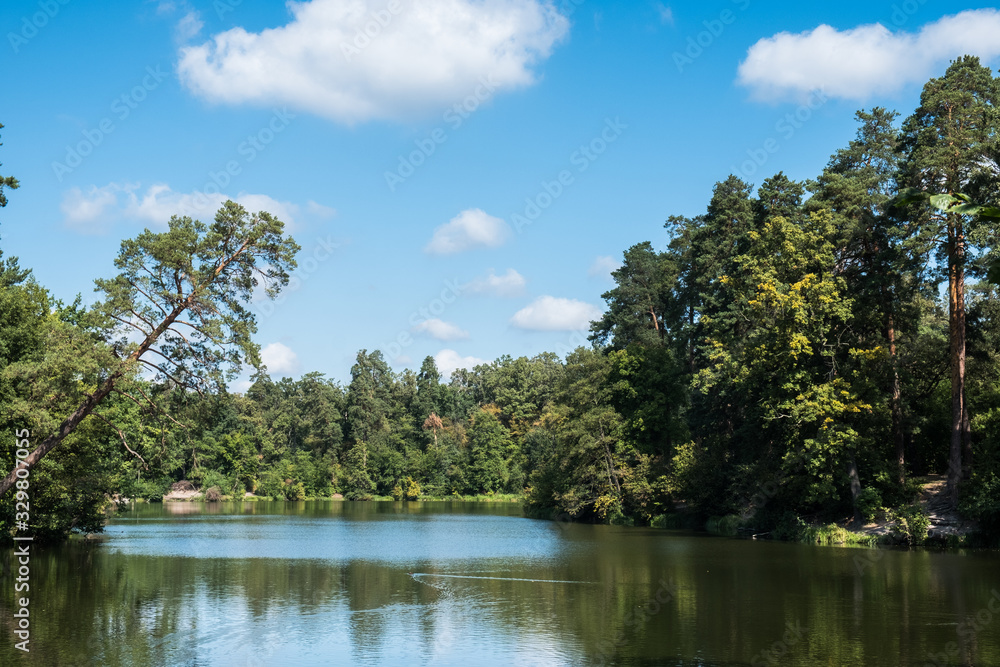 Fototapeta premium Scenic view of the park in the center of the big city in the summer. With a lagoon in the middle and green trees. In the atmosphere of evening light