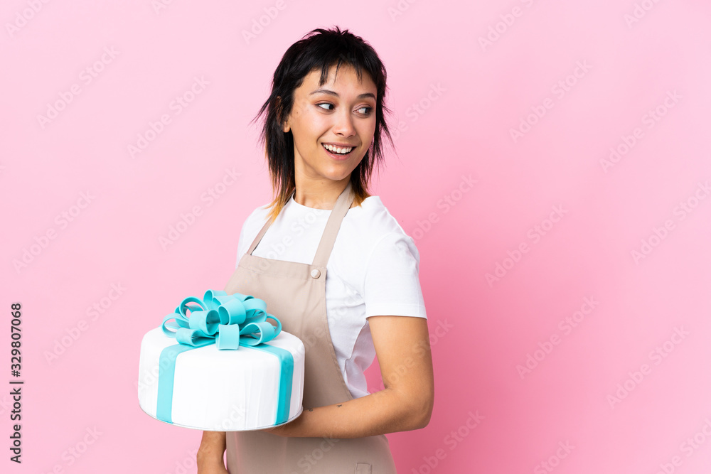 Uruguayan Pastry chef holding a big cake over isolated pink background laughing Uruguayan Pastry chef holding a big cake over isolated pink background laughing