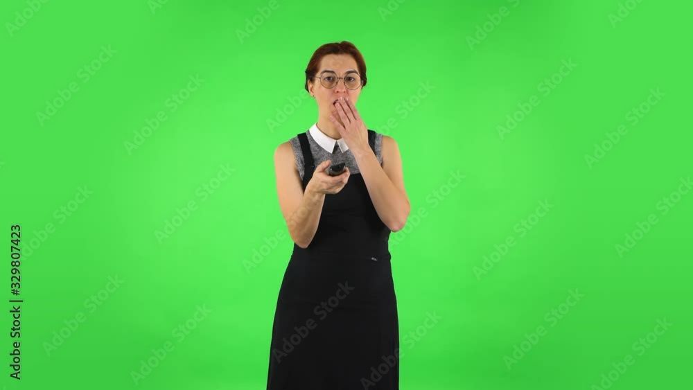 Funny girl in round glasses with TV remote in her hand, switching on TV. Green screen Funny girl in round glasses with TV remote in her hand, switching on TV. Green screen